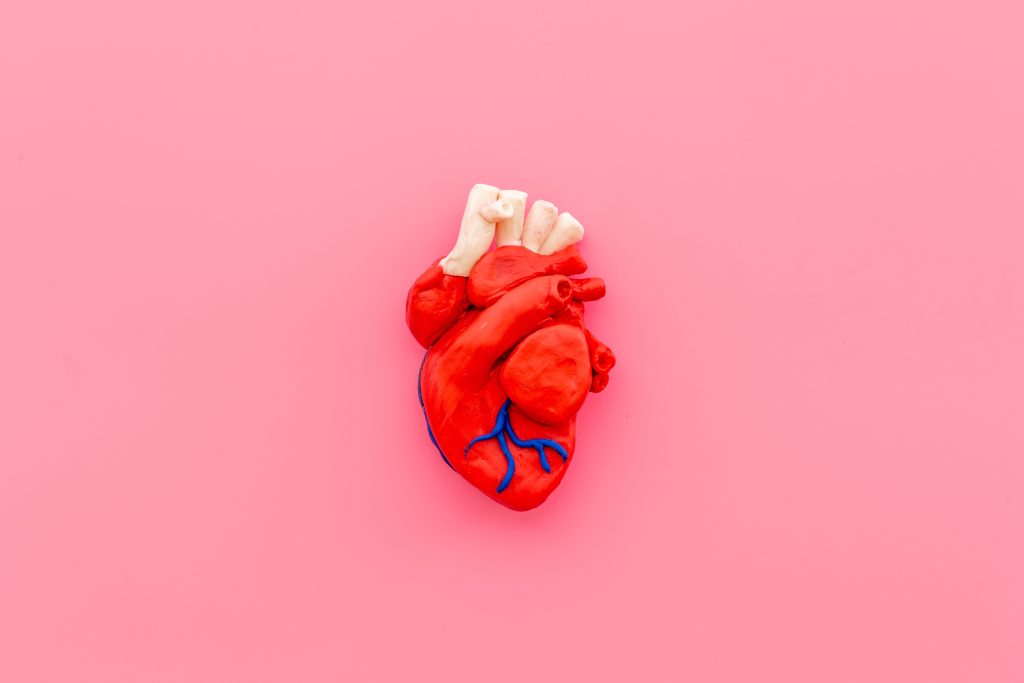 human heart made of clay on a pink background